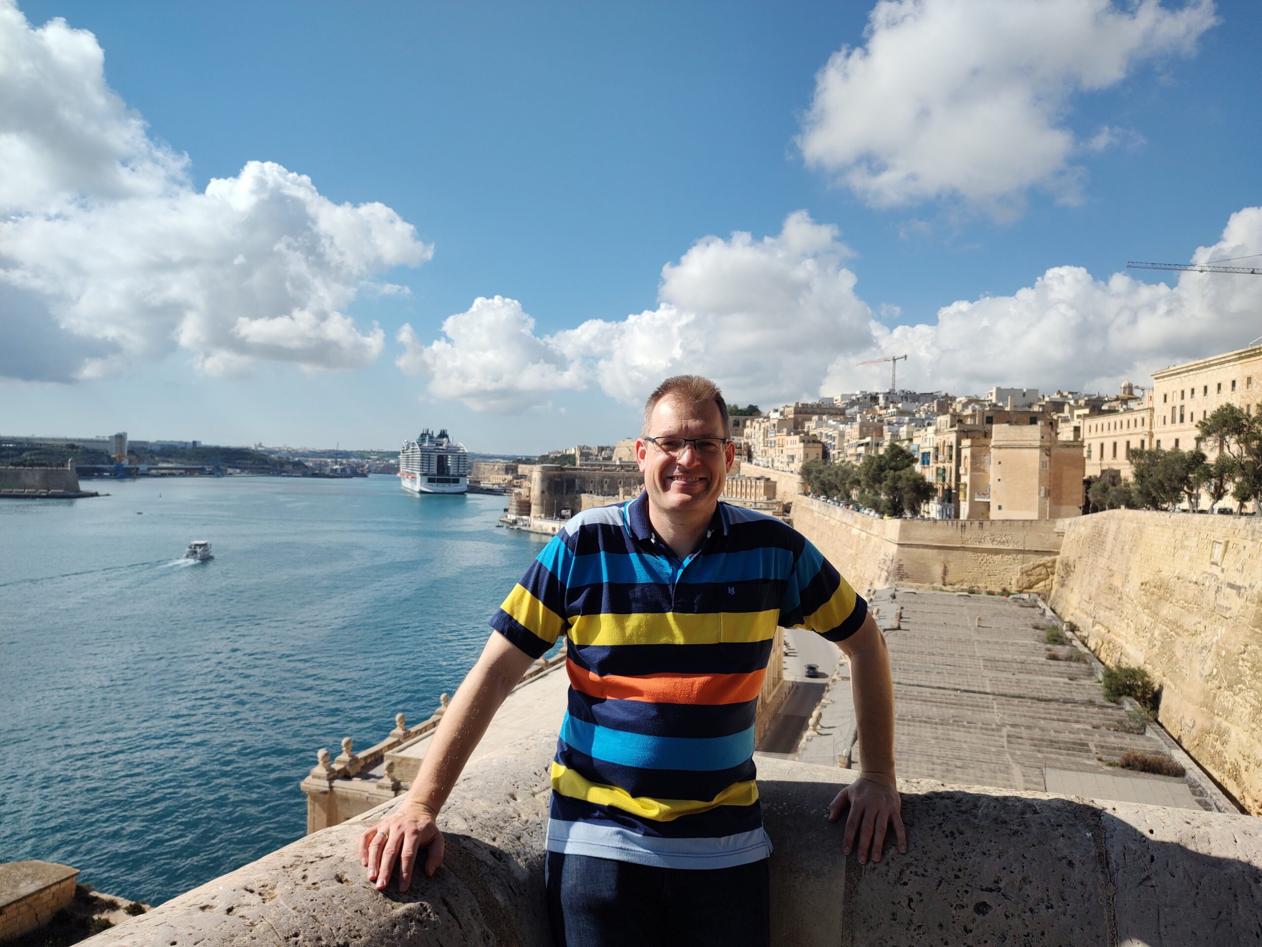 Stefan Mehlgarten steht an einer Mauer in Valletta Malta und im Hintergrund liegt MSC World Europa
