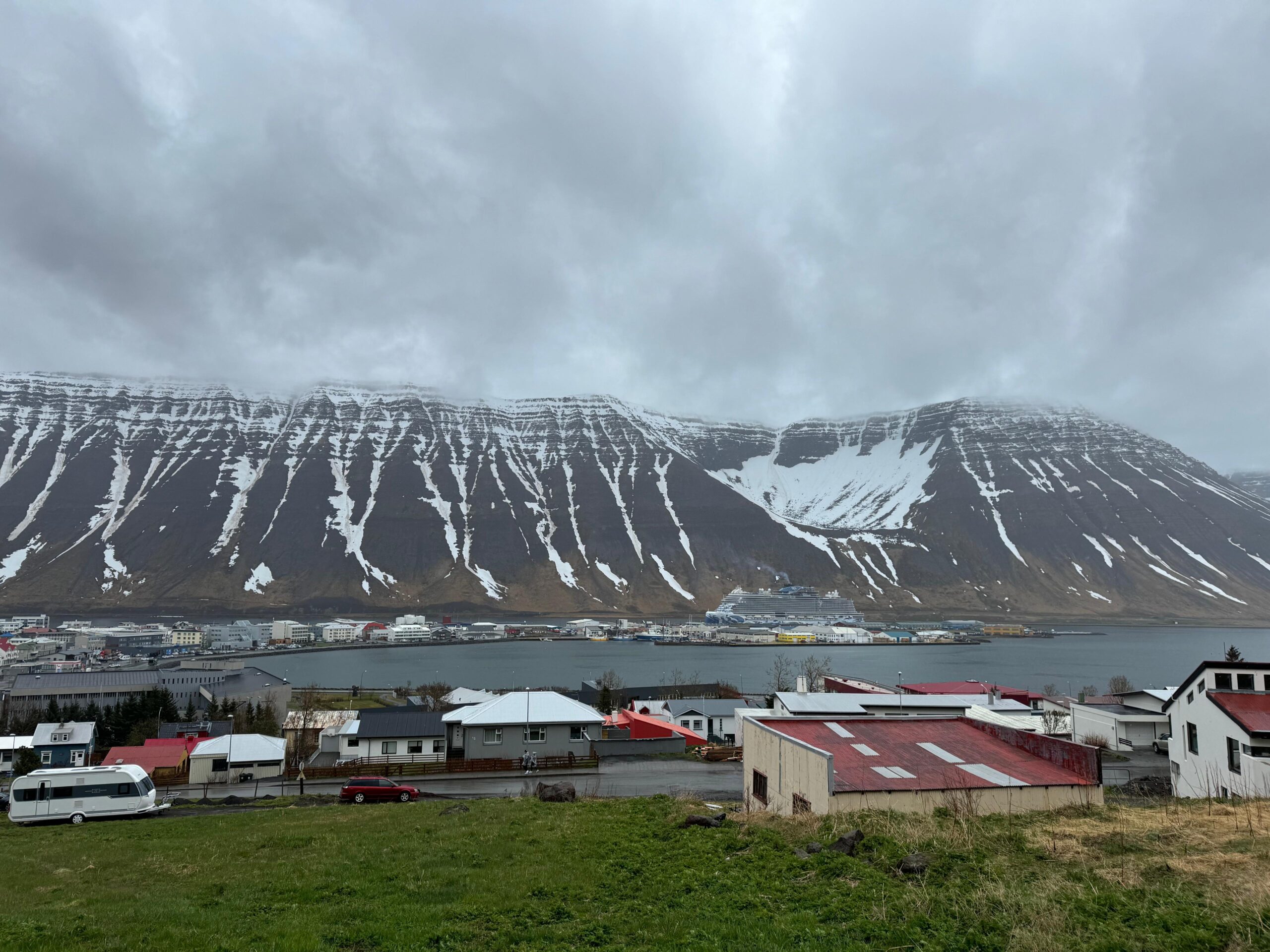 Blick auf den Hafen von Ísafjörður in Island mit schneebedeckten Bergen, einem Kreuzfahrtschiff und Häusern im Vordergrund.